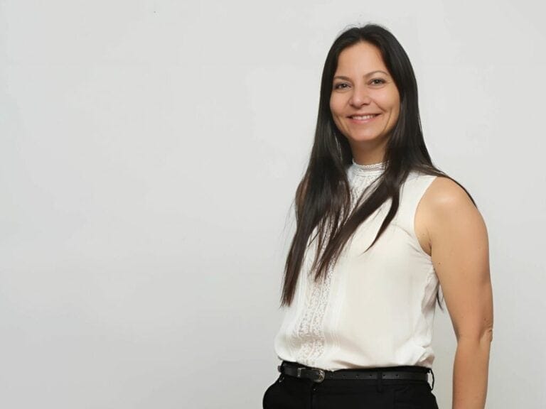 אישה עם שיער כהה ארוך מחייכת, לובשת חולצה לבנה ללא שרוולים, ועומדת על רקע רגיל, מגלמת את החום והפתיחות של מטפלת המוכנה לאמץ כל רגע של הקשבה. | גליה גביש מטפלת LI-CBT ילדים, נוער ומבוגרים ומדריכת הורים