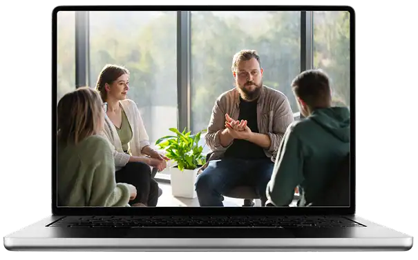 מסך מחשב נייד מציג ארבעה אנשים היושבים במעגל, עוסקים בדיון קבוצתי בחדר מואר עם חלונות גדולים ועציץ. | גליה גביש מטפלת LI-CBT ילדים, נוער ומבוגרים ומדריכת הורים